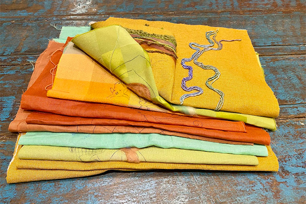 Retalhos para aplicação em bordados. Uma série de retalhos de tecido, todos de tom terossos, empilhados uns sobre os outros.